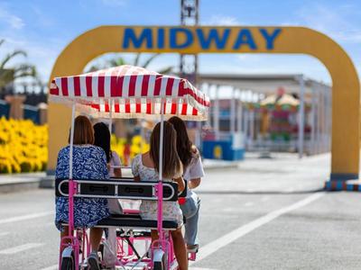 Deux personnes roulent sur un vélo à quatre roues devant une arche jaune MIDWAY.