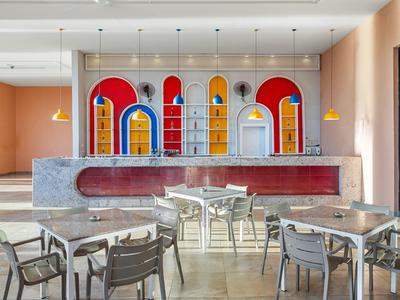 Area pranzo moderna con design murale colorato e tavoli con sedie in metallo e legno.