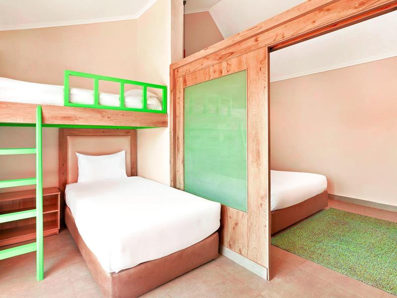 Camera d'albergo con letto singolo, letto a castello verde, specchio e tappeto verde.