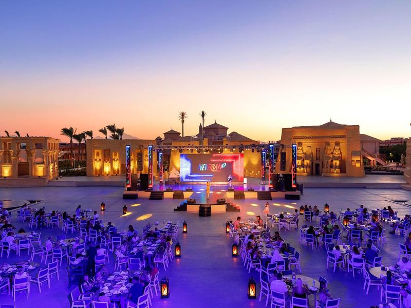 Cena all'aperto con palco e tavoli illuminati al tramonto.