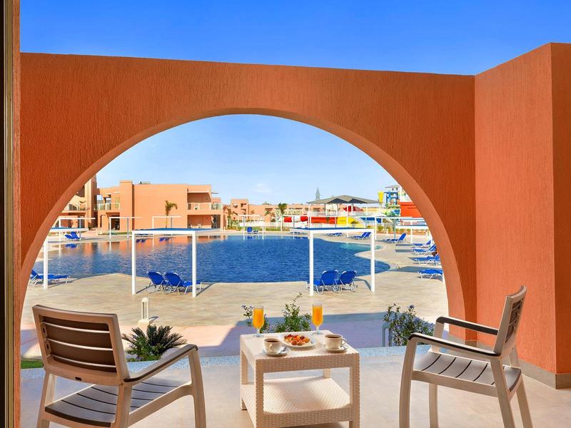 Terrazza con vista su porto soleggiato, due sedie e tavolo con bevande.