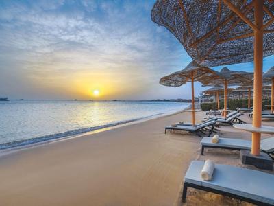 Sonnenuntergang am Strand mit Liegestühlen und Sonnenschirmen am Meer.