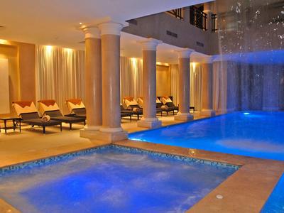 Innenpool mit blau beleuchtetem Wasser, Relaxliegen, weißen Säulen und warmem Beleuchtungsschein.