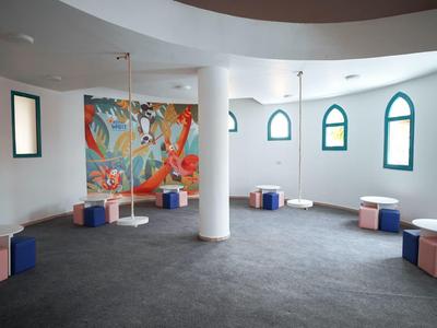 Stanza curva con sgabelli colorati, finestre ad arco e un murale vivace.