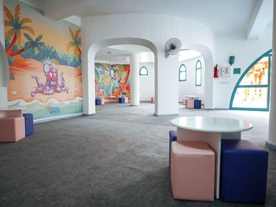 Sala giochi luminosa con murales colorati, moquette morbida e piccoli pouf cubici.