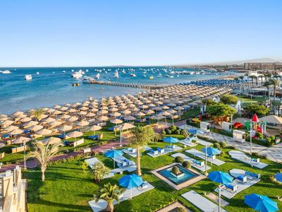 Plaża z parasolami, marina i zielone tereny ośrodka wypoczynkowego.