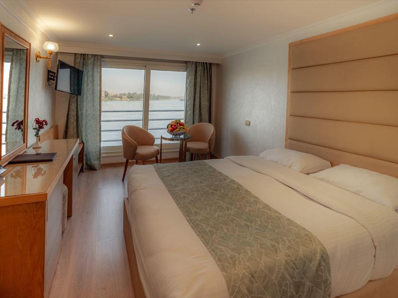 Elegancki pokój hotelowy z dużym łóżkiem, fotelami i jasnym balkonem.