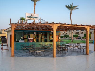 Open bar and seating area with tables and chairs under pergola, palm trees in background.