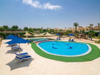 Round pool with blue loungers and umbrellas in a sunny hotel area.