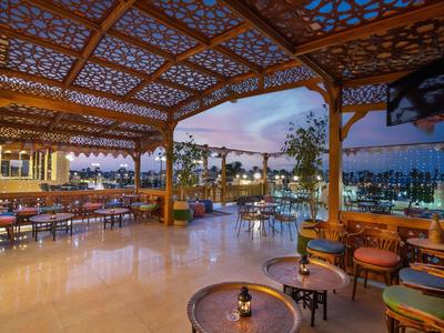 Open seating area with wooden furniture overlooking a lit pool at sunset.