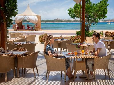 Two women sit at an outdoor table overlooking the beach and sea.