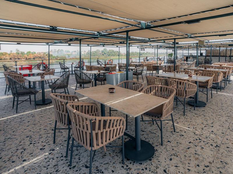 Spacious outdoor dining area with modern chairs and tables under a large canopy by the water.