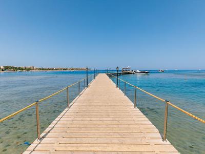 Pontile in legno con ringhiera che si estende su acqua limpida verso l'orizzonte sotto un cielo blu.