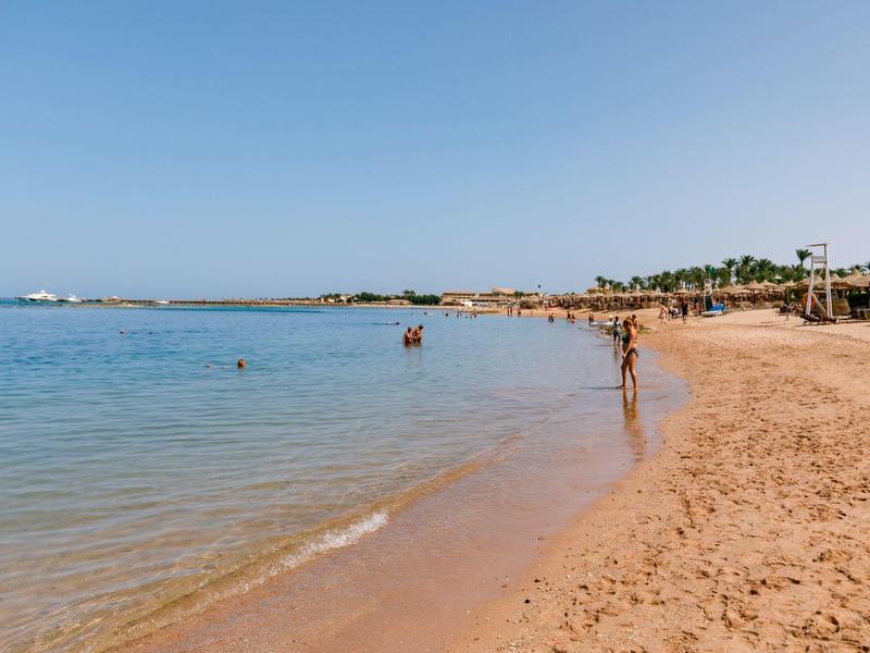 Plage tranquille avec sable doré, eau claire, ciel bleu et quelques vacanciers.
