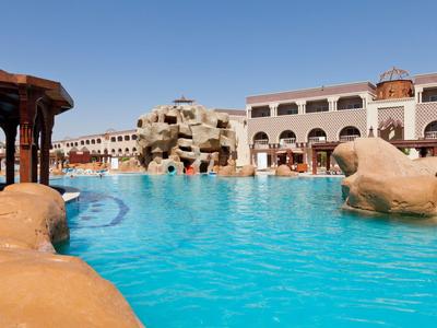 Großer Hotelpool mit Felsen und Wasserfall unter klarem blauem Himmel.