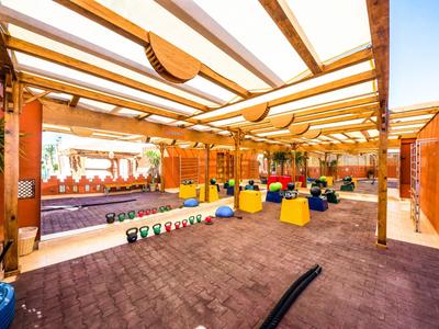 Offener Fitnessbereich mit Kettlebells und Sitzgelegenheiten unter einem Holzpergola-Dach.