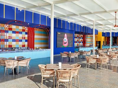 Moderner, offener Gastraum mit bunten Wänden, Holzstühlen und Tischen unter weißem Dach.