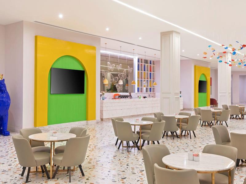 Moderner Essbereich mit runden Tischen, grauen Stühlen und buntem Kunstwerk an weißer Decke.