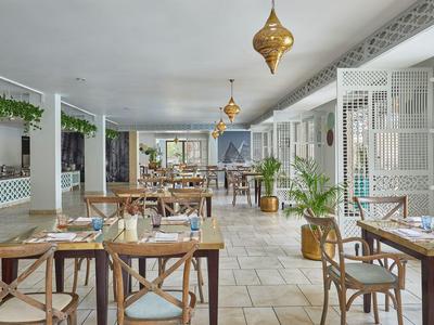 Helles Restaurant mit Holztischen, Pflanzen und modernen goldenen Hängelampen.