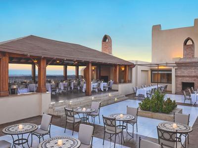 Terrasse eines Hotels mit Sitzgelegenheiten, Kamin und Blick auf das Meer bei Sonnenuntergang.