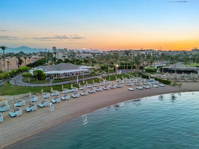 Plage avec transats, pavillons et horizon de la ville au coucher du soleil.