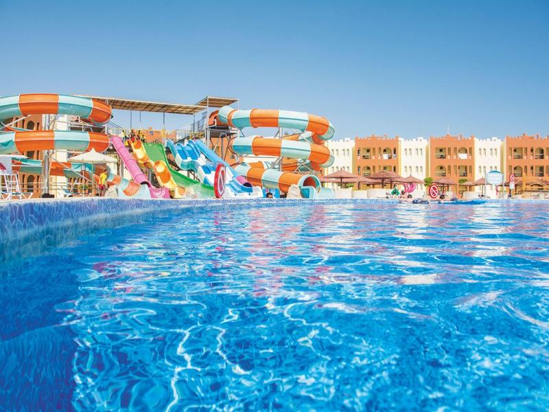 Blauer Pool mit Wasserrutschen und Hotelgebäuden im Hintergrund unter klarem Himmel.