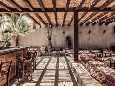 Halboffener Lounge-Bereich mit Holzdach, Bänken und Bar unter Sonnenlicht.