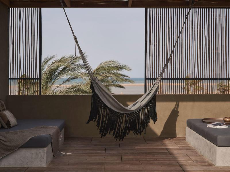 Hängematte auf Balkon mit Sofa, Stuhl und Palmen im Hintergrund.