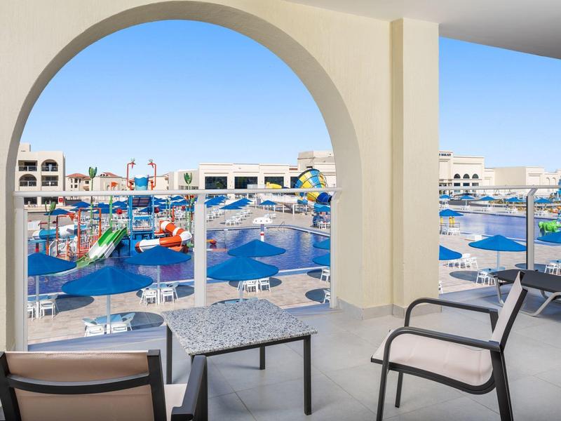 Balkon mit Blick auf Pool und Sonnenschirme in einem Hotelresort.