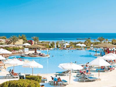 Grande piscine d'hôtel avec parasols et chaises longues au bord de la mer sous un ciel clair