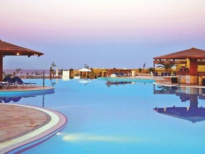Grand piscine avec parasols et clients se détendant dans un complexe hôtelier au coucher du soleil.