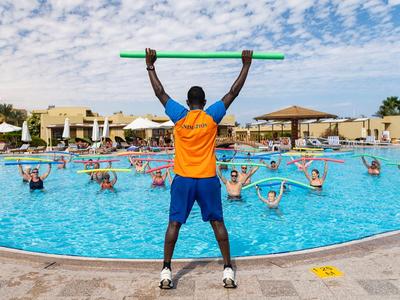 An instructor leads a water aerobics class in a hotel pool, participants lifting colorful pool noodles.