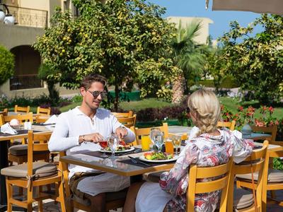 Coppia che gode di una colazione all'aperto al sole in un ristorante con giardino e alberi di arancio.