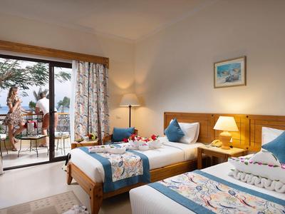 Chambre d'hôtel confortable avec deux lits, porte de terrasse et vue sur un paysage enneigé.