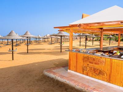 Ein Sandstrand mit Sonnenschirmen und einem Holzkiosk mit Speisen unter klarem Himmel.