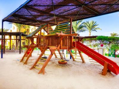 Kinderspielplatz mit Klettergerüst und Rutsche unter einem schattigen Dach in einem Hotelbereich.