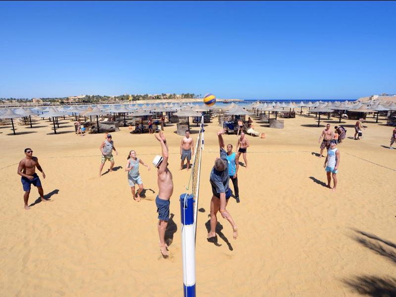 Menschen spielen Volleyball auf einem sonnigen Sandstrand am Meer.