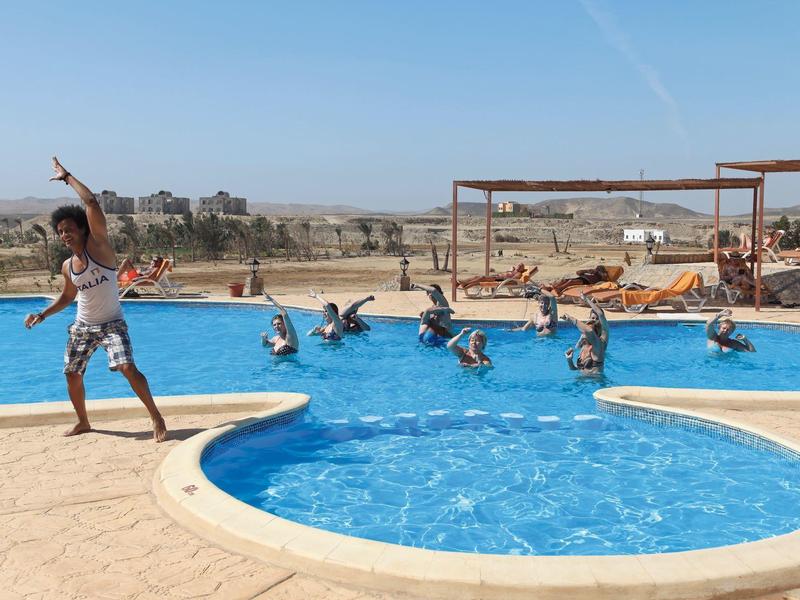 Persone che si divertono in una piscina rotonda con area bambini sotto un cielo sereno.