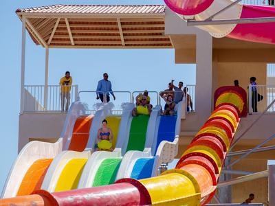Several people wait at the top of colorful water slides under a clear sky.