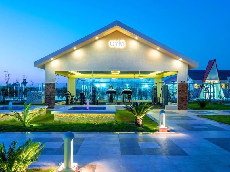 Ingresso elegante di un hotel illuminato al crepuscolo con piante e percorso lastricato.