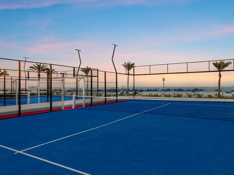 Campo sportivo blu all'aperto con vista sul mare al tramonto.