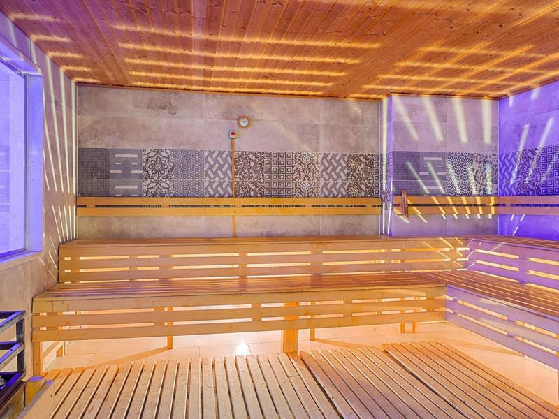 Interno illuminato di una sauna in legno con panche e luci viola.