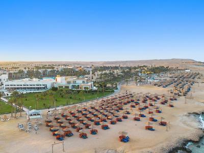 Strand met veel parasols naast een hotelcomplex bij helderblauwe zee.