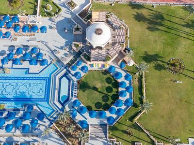 Vista aérea de un hotel con piscina azul, sombrillas y césped verde adyacente.
