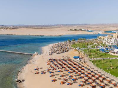 Strand met parasols en ligbedden naast een hotel en helder blauw water onder een blauwe lucht