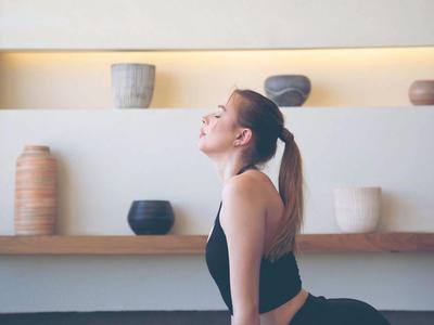 Frau praktiziert Yoga auf blauer Matte vor einer Wand mit Regalen und Töpferwaren.