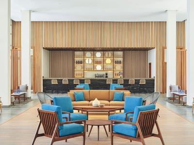 Moderner Lounge-Bereich mit blauen Sesseln und einer Bar im Hintergrund in einem Hotel.