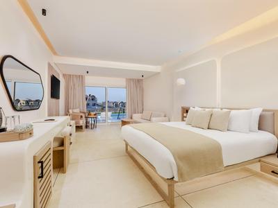 Habitación de hotel luminosa con cama grande, escritorio, espejo y balcón con vista al mar.