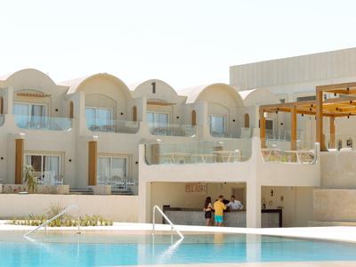 Hotel con piscina, fachada blanca y balcones con arcos a la luz del día.