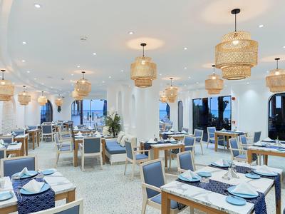 Ristorante spazioso con decorazioni blu e bianche e lampade a sospensione in rattan.